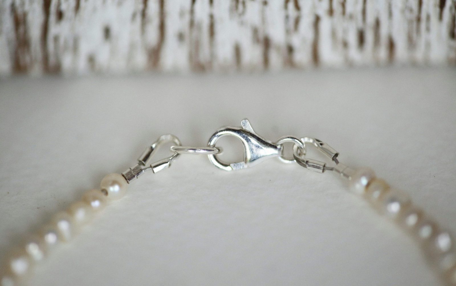 Close-up of a silver clasp on a luxury pearl necklace against a white surface.