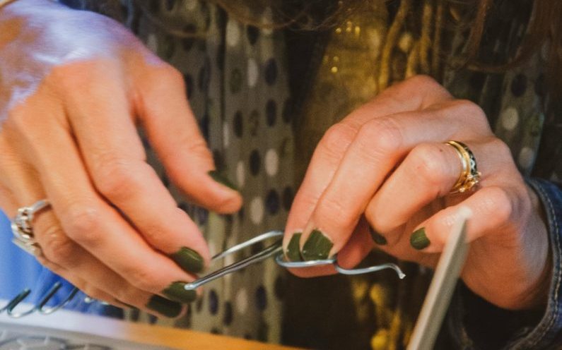 Close-up of hands crafting wire art in a warm workshop environment, featuring a variety of tools and materials on a desk.